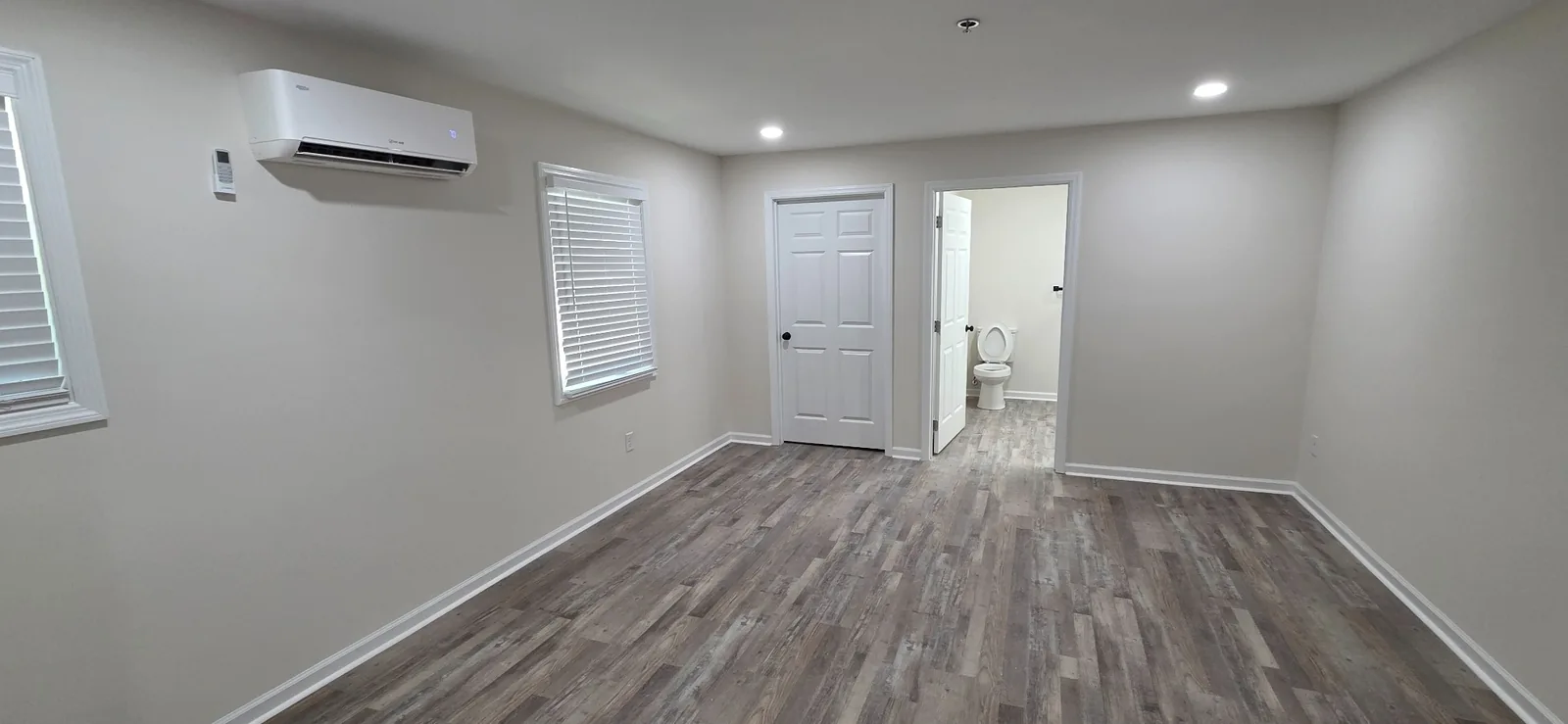 A Marlboro living space with a mini-split unit, window blinds and a doorway through to the bathroom.