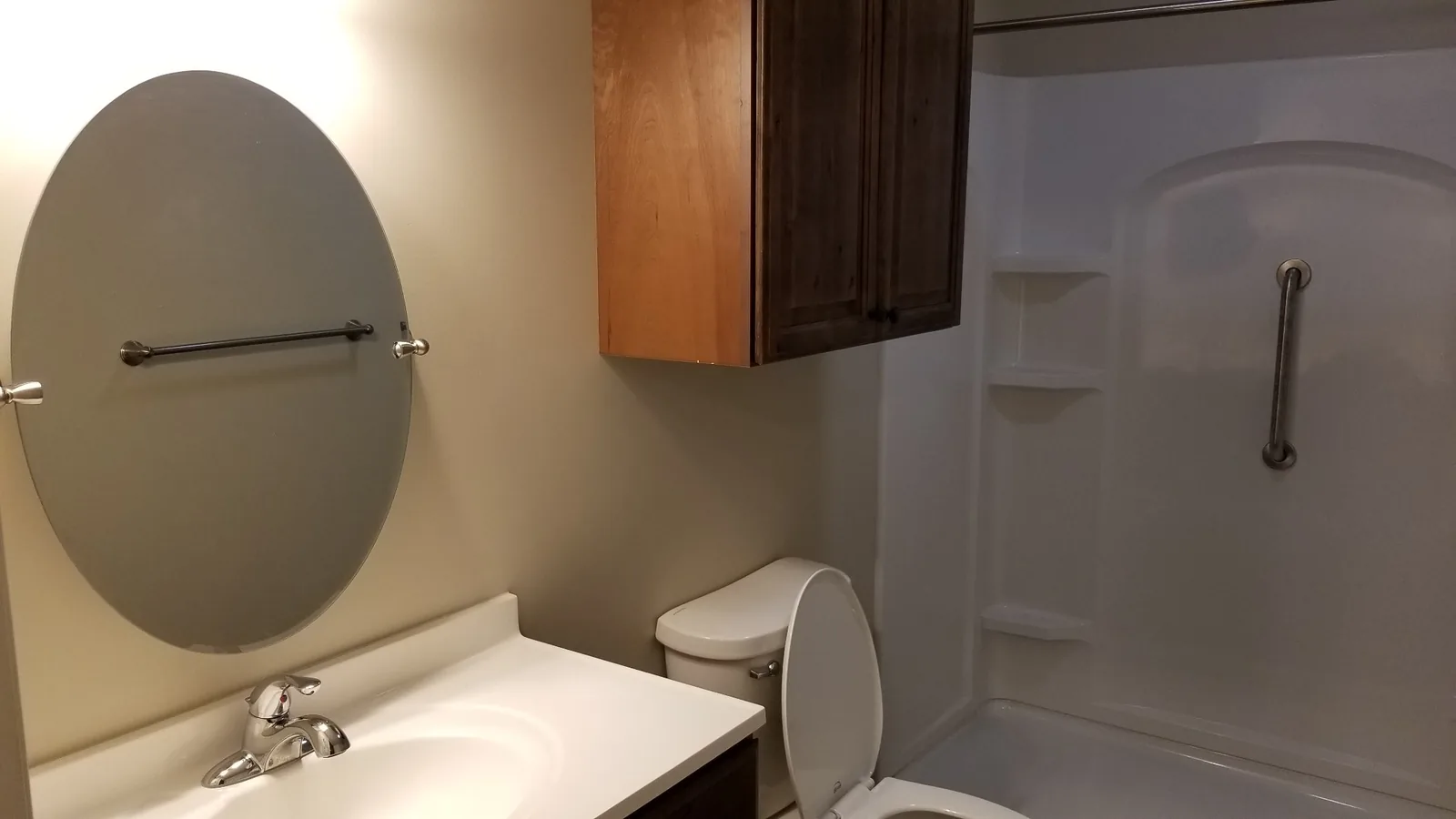 Bathroom vanity with a tilting mirror, grab bar and storage cabinet above.