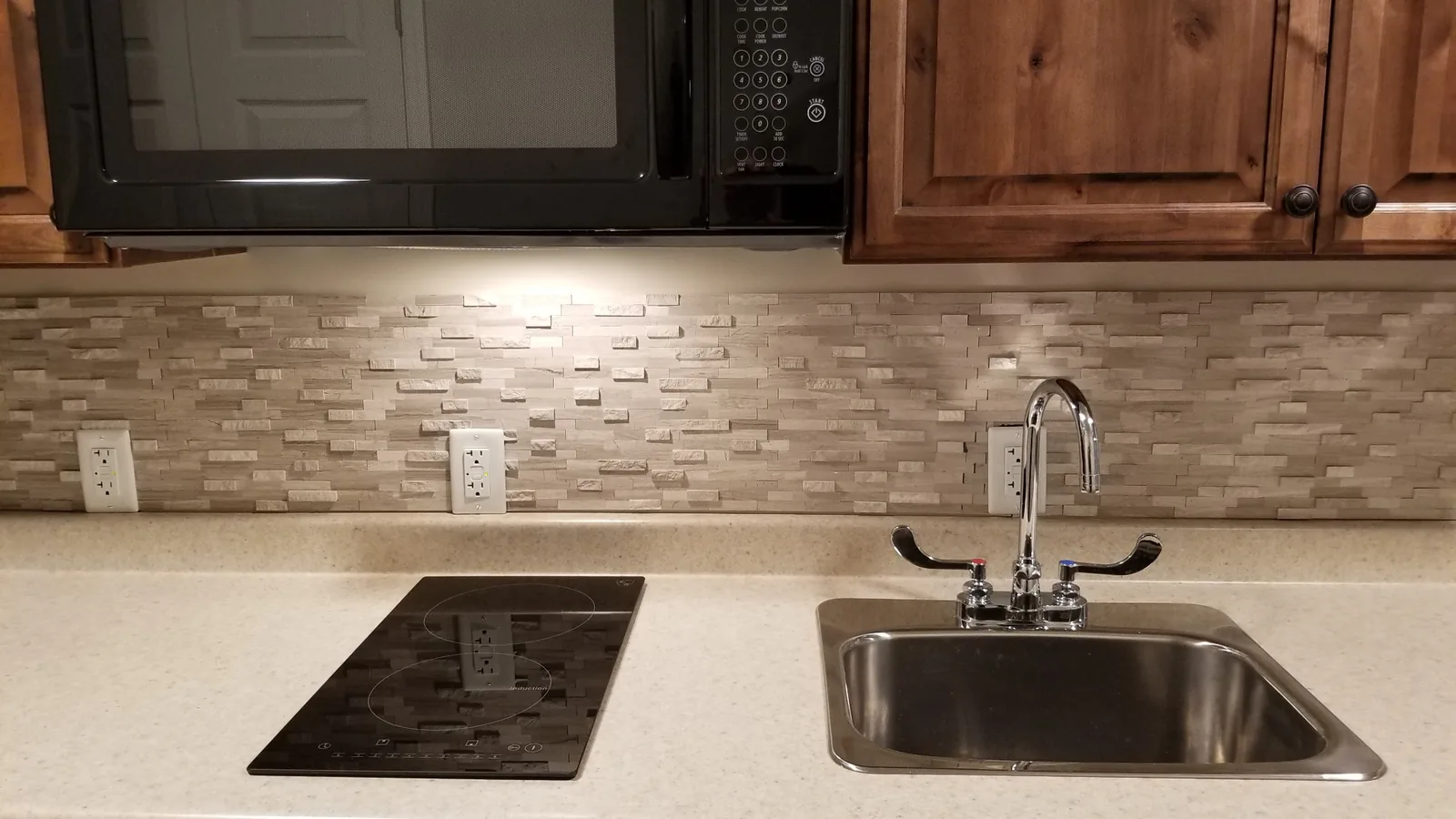 Close view of a stainless sink, two-burner cooktop and tile backsplash.