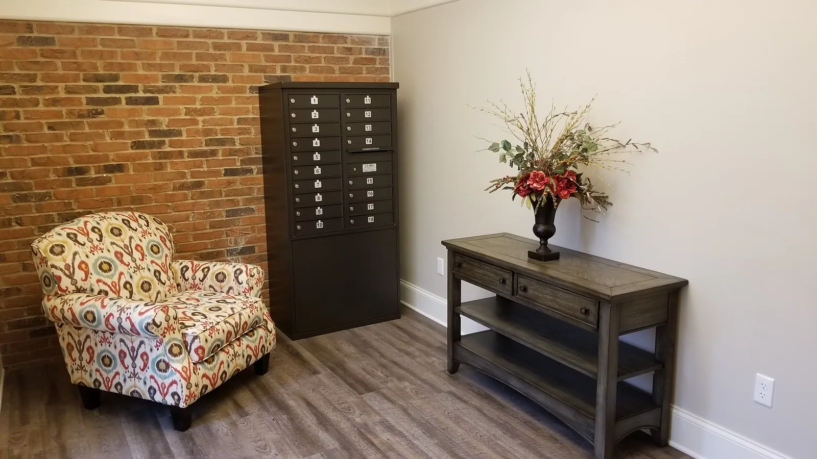 A bank of resident mailboxes beside a console table and an upholstered armchair.
